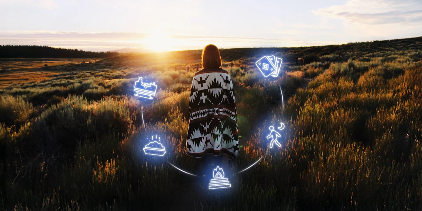 Femme enveloppée d’un châle observant le coucher du soleil, entourée de symboles lumineux représentant des rituels spirituels d’Halloween pour célébrer le passage et le renouveau intérieur.